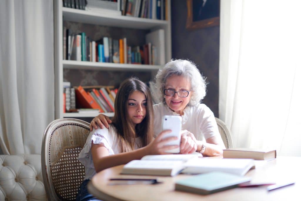 One elderly woman and one girl are sitting around a table, looking at a mobile phone